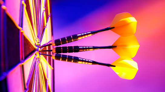 Three back and yellow darts sunk into the center of a dartboard on a purple-pink background, to represent defining a brand