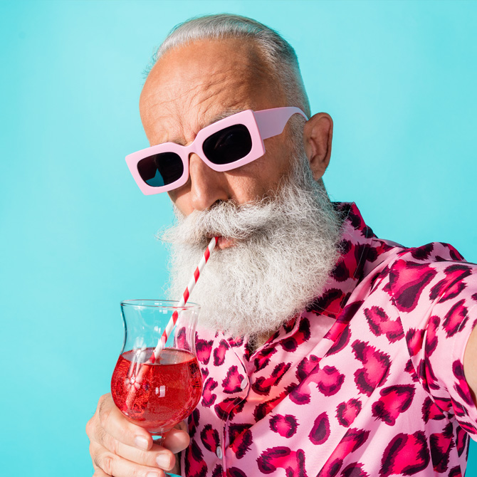 A bold, fun senior man with a white mustache and beard in a wild, bright oink, cheetah print shirt, with pink sunglasses, and a bright, fruity cocktail owning a distinct and unique brand