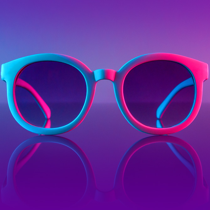 Bright blue and pink sunglasses on a purple background representing the lens of a brand refresh