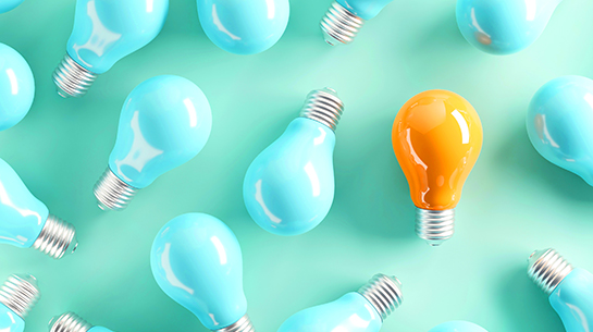 A bright yellow light bulb (representing a new idea) surrounded by teal light bulbs on a teal background
