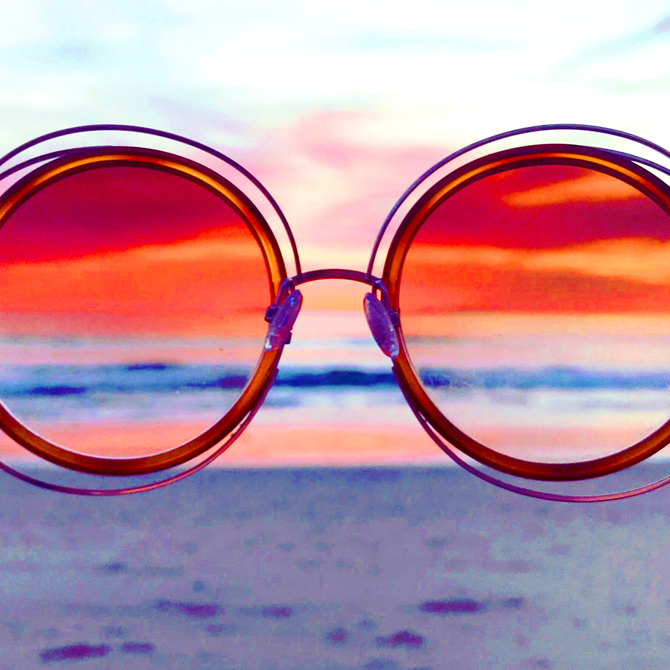 A pair of round-lensed, rose-colored glasses providing a clear picture and understanding of the landscape ahead (a beach and the ocean)