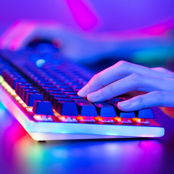 A web designer designing a business website in a low-light, purple room, using a keyboard lit with rainbow lights