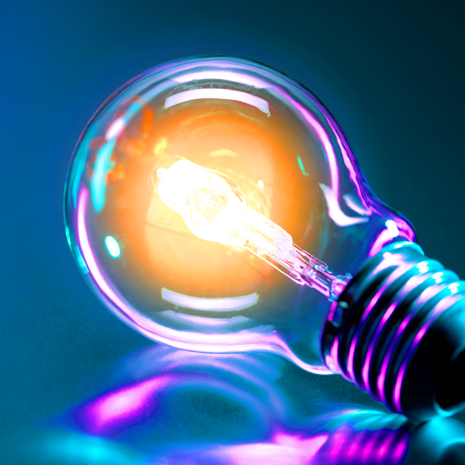 A bright light bulb with a purpleish-pink glare on a blue background, illuminating project details